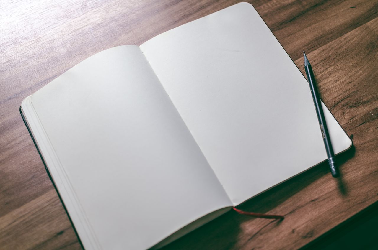 Home An open sketchbook with blank pages and a pencil on a wooden desk, offering creative potential.